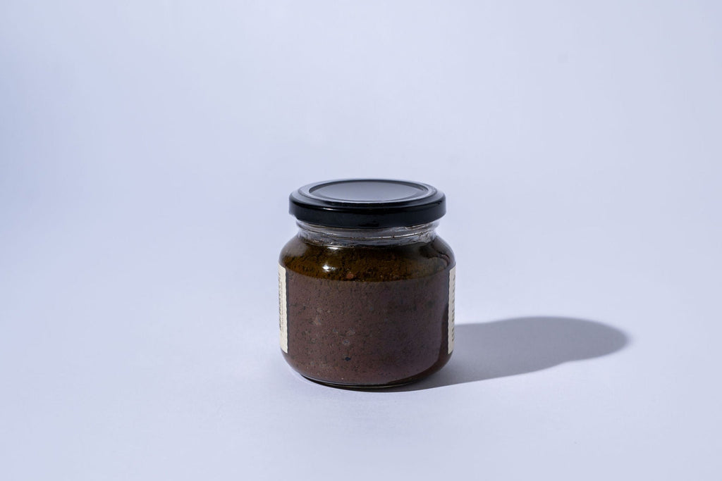 Small jar of black olive spread with a black lid on a white background