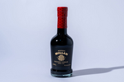 Bottle of Millan balsamic vinegar with a red cap on a light gray background