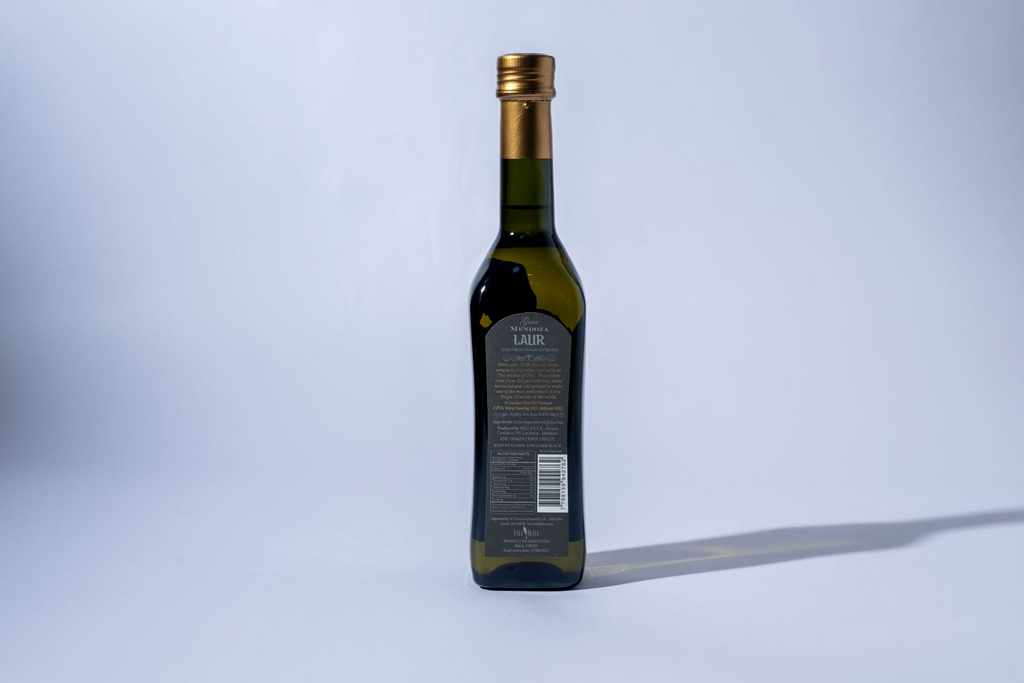 Bottle of olive oil with a gold cap on a light gray background with black label
