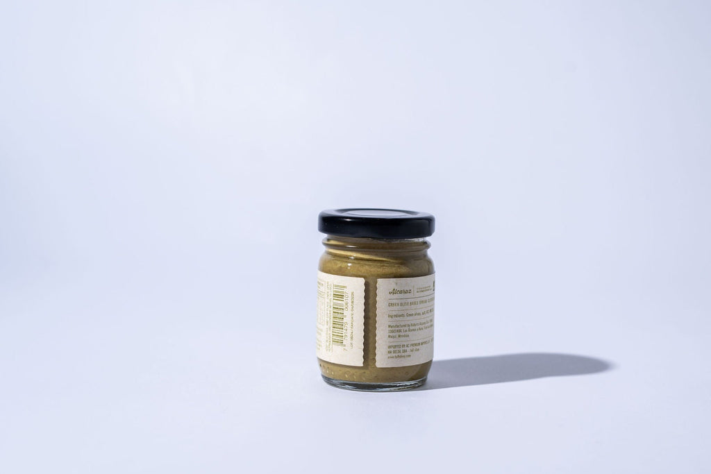 Small jar of green olive spread with a label on a light purple background