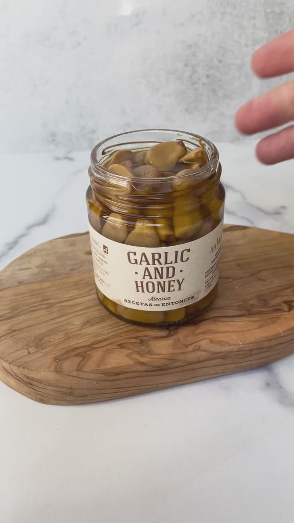 A jar of whole garlic cloves combined with honey, showcasing the natural textures of the garlic and the golden color of the honey being placed on a cracker