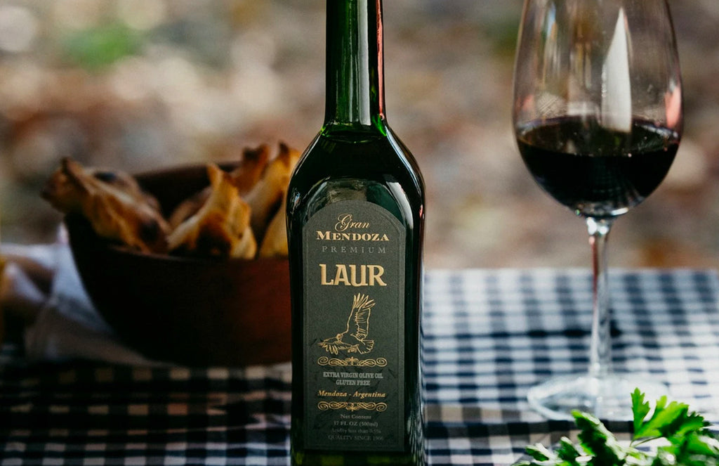 Green Bottle of Gran Laur Extra Virgin Olive Oil on a blue checkered table cloth next to glass red wine